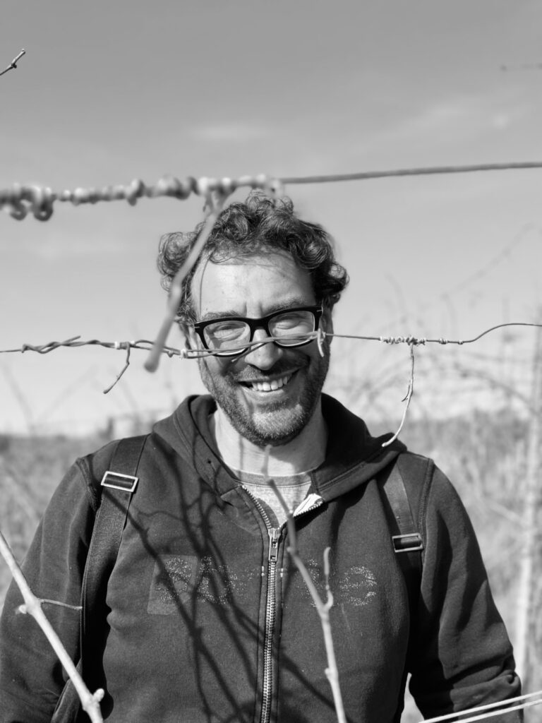 Daniele Tinti, titolare dell'azienda ritratto durante il lavoro di potatura della vite nei suoi vigneti. La foto è in bianco e nero e Daniele è sorridente e appagato dal suo lavoro!